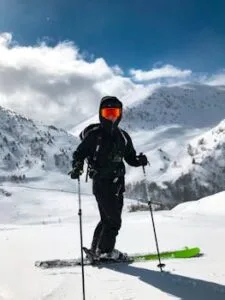 Energetic skier in black gear enjoying snowy slopes under blue sky and sunlight.